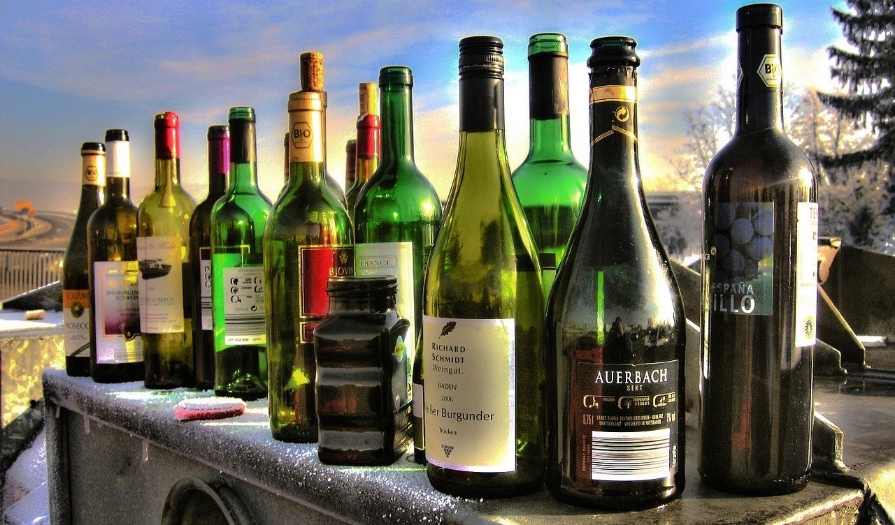 Sechszehn verschiedenfarbige Glasflaschen stehen auf einem Müllcontainer im Winter.