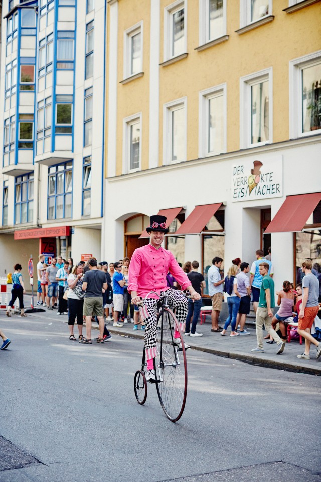 Ein Mann mit vielen Talenten: Auch Hochradfahren zählt dazu. Im Hintergrund ist die lange Warteschlange seiner Gäste zu sehen (Foto: Der verrückte Eismacher)