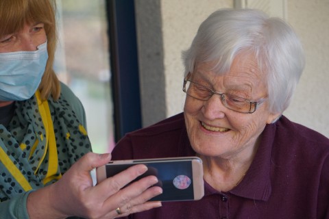 Frau mit Maske zeigt älterer Frau Smartphone