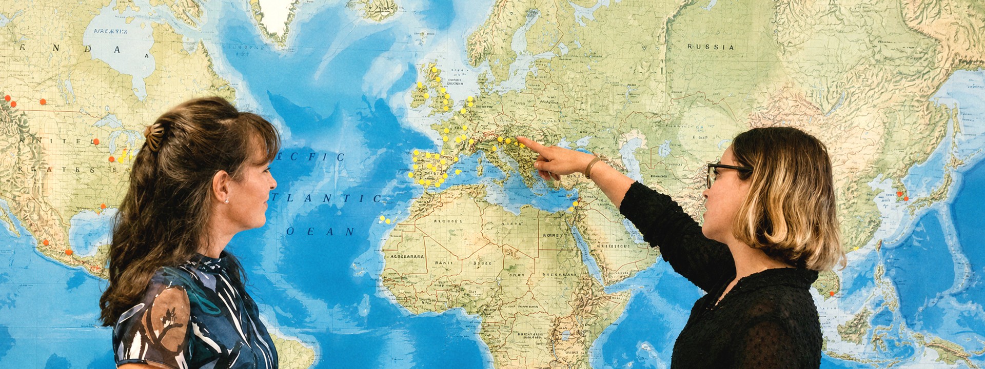 Two woman standing infront of a world map 