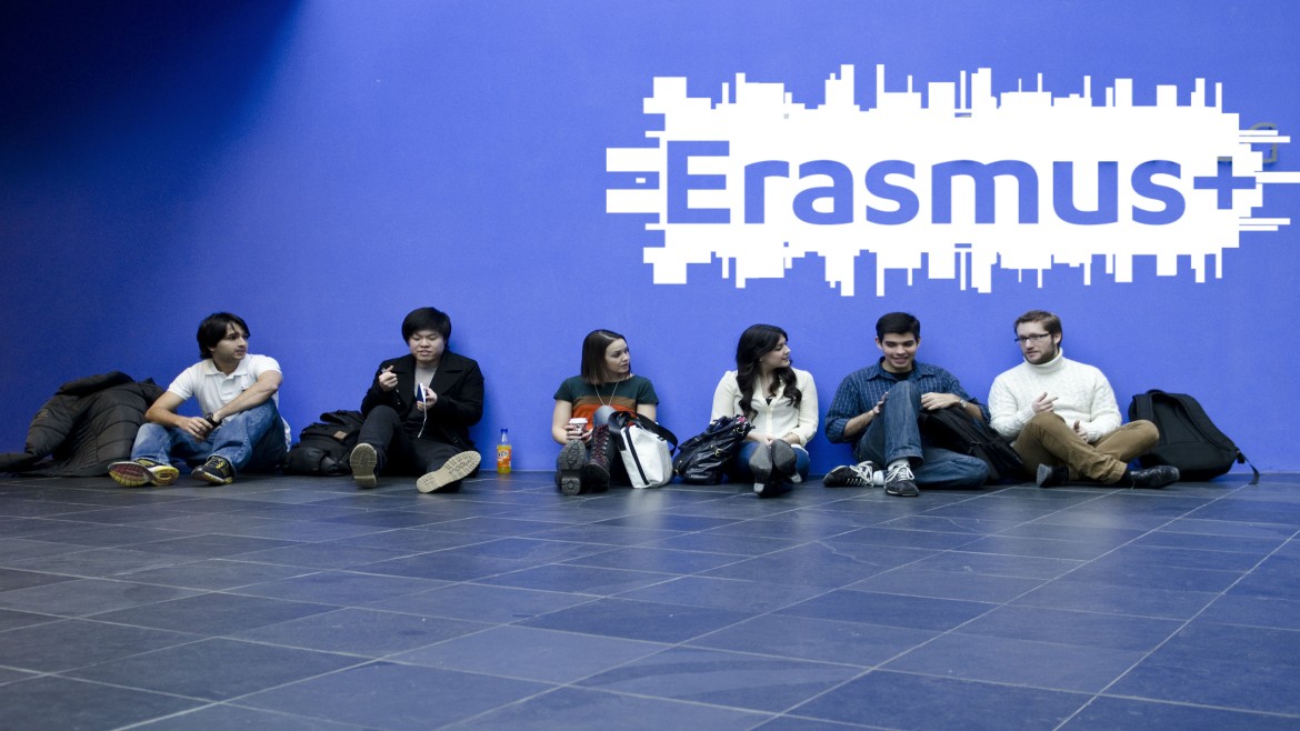Group of students sitting in front of a blue wall with Erasmus+ written on it.