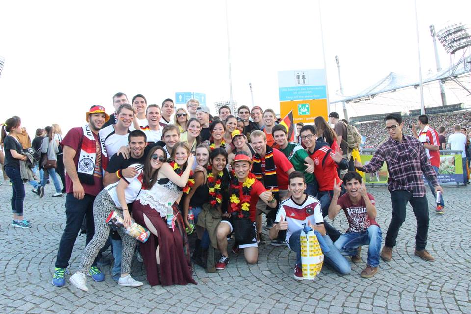 Students in front of the arena at a German soccer game, dressed in various decorative items from the German soccer team
