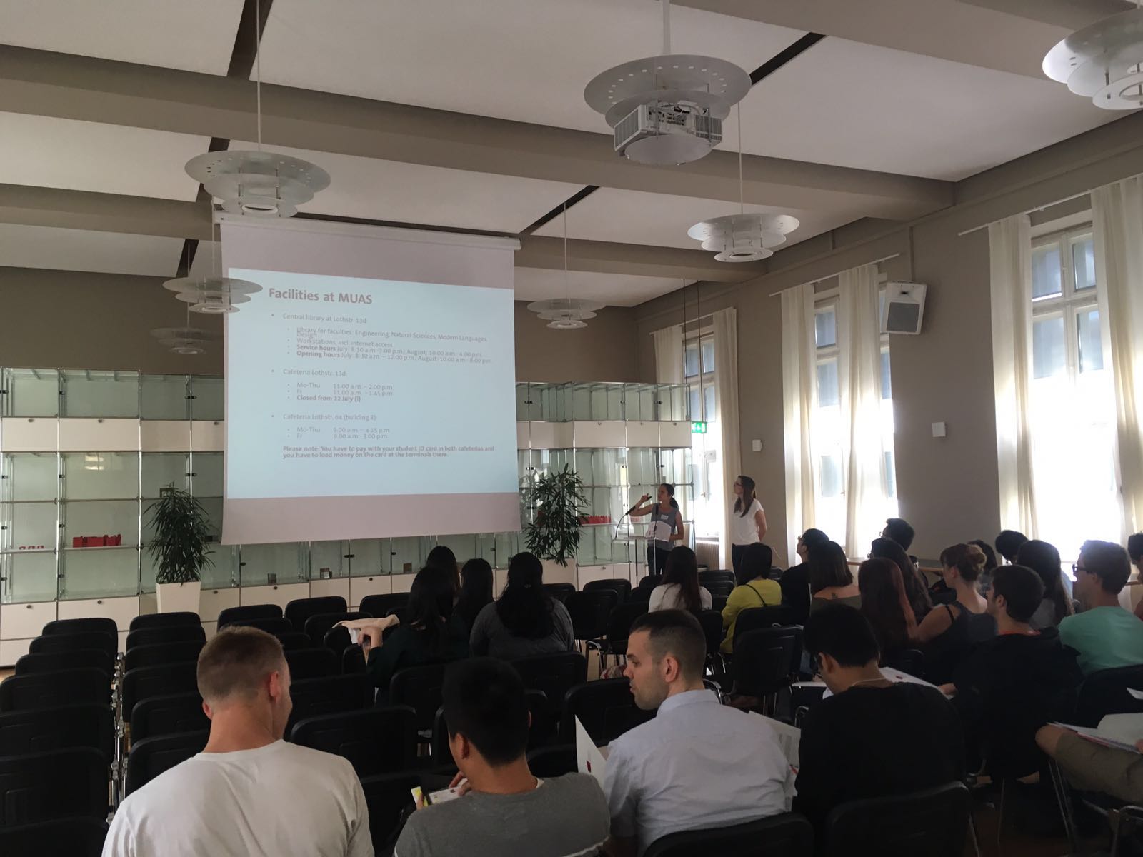 Students sitting in the Oskar von Miller Hall of the Munich University of Applied Sciences on Welcome Day, Ms. Vasil standing in front and assisting in giving the presentation about the summer school