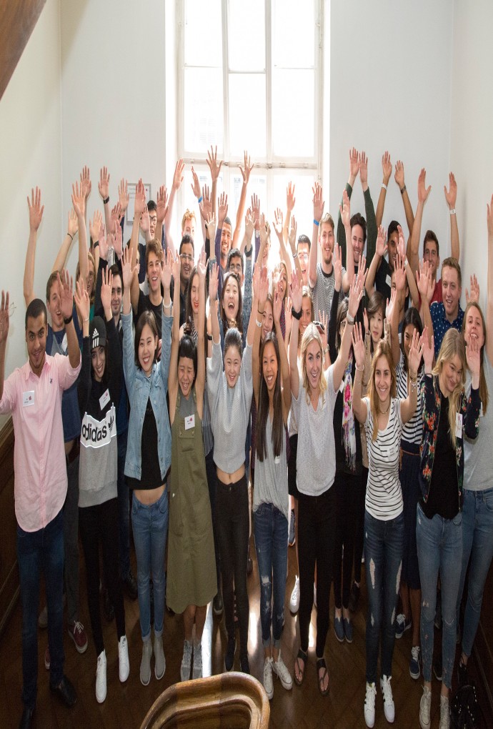 Summer school students smiling in the old building of the Munich University of Applied Sciences, with their hands raised up the air