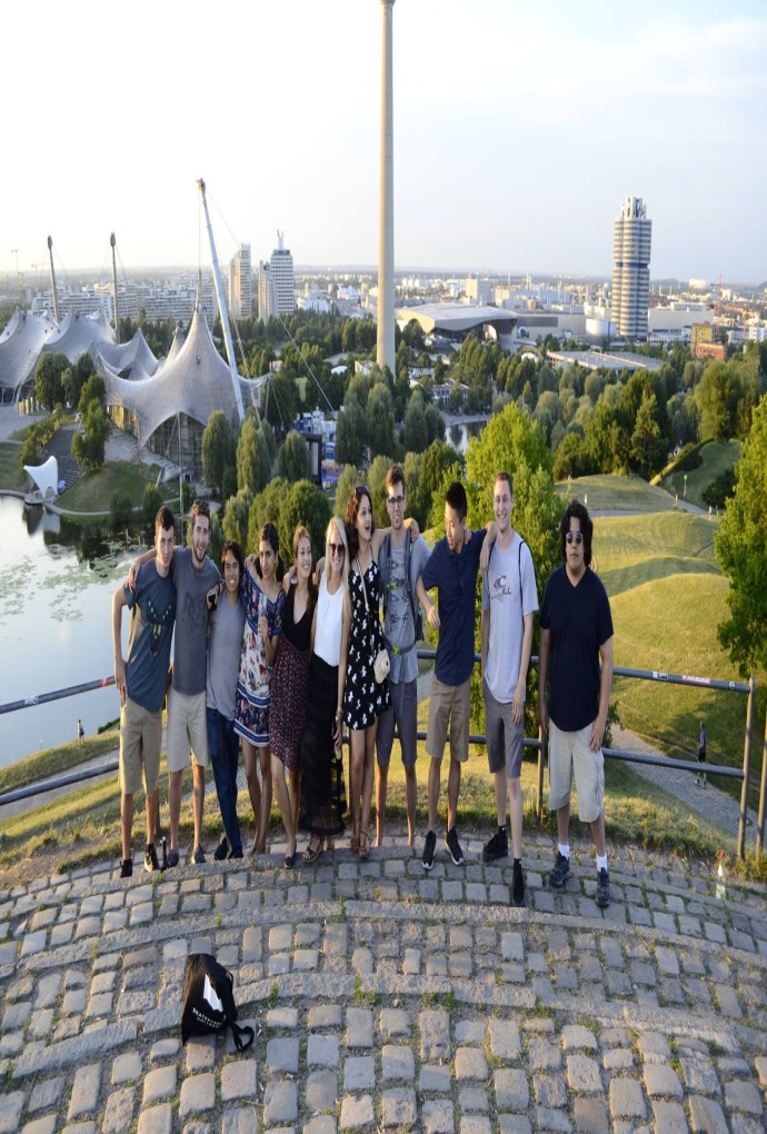 Summer school students on the Olympiaberg in the Olympiapark, in the background the Olympiaturm, Olympiasee and trees can be seen, also the backdrop of the city.