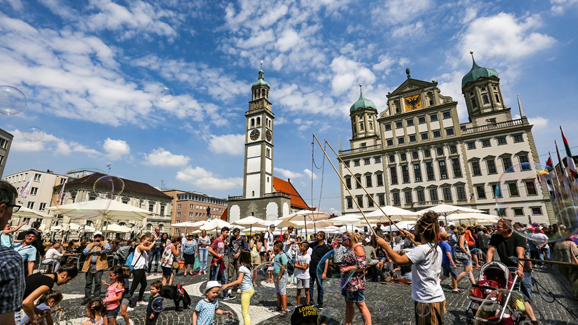 Augsburg am Tag, zu sehen ist die Altstadt mit vielen Menschen, im Hintergrund das Rathaus 