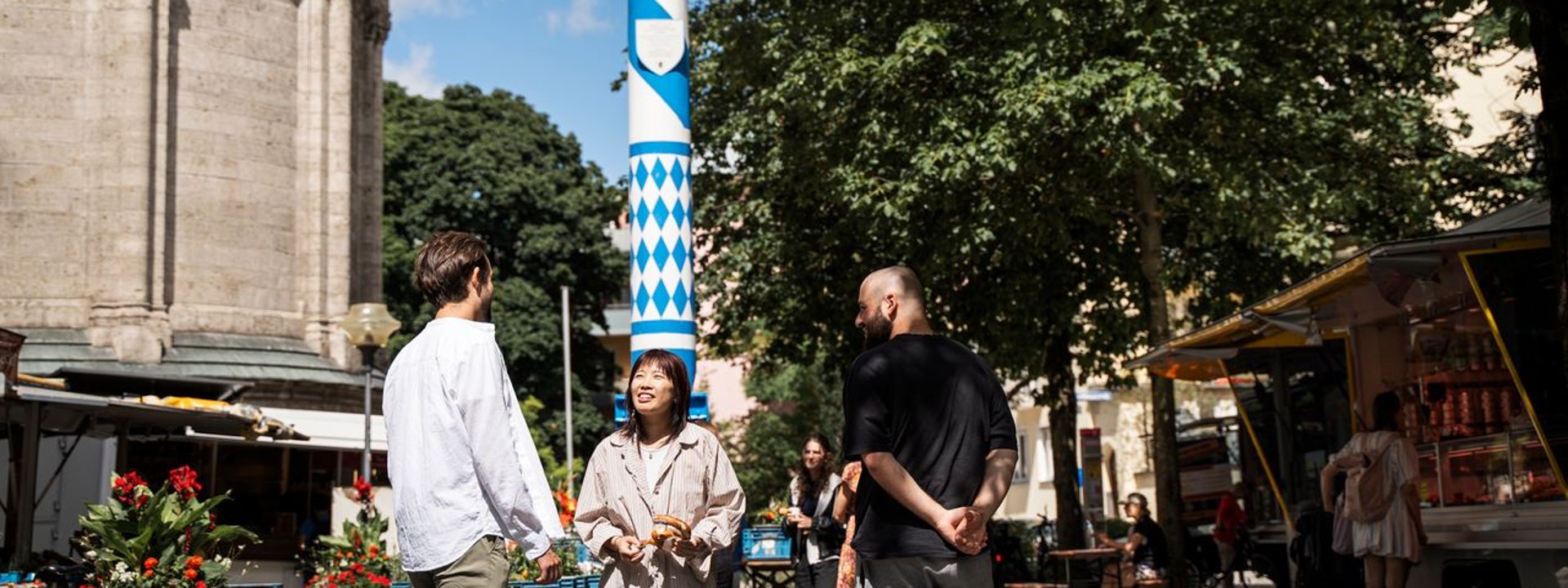 Studierende der Hochschule München stehen auf einem Marktplatz vor dem Maibaum
