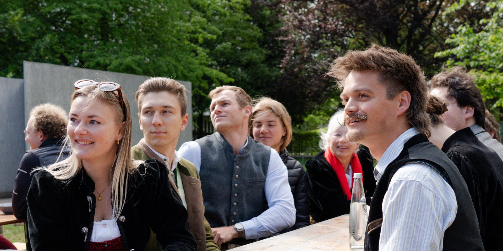 Studierende der Hochschule München sitzen an einer Bierbank auf dem Maibaumfest