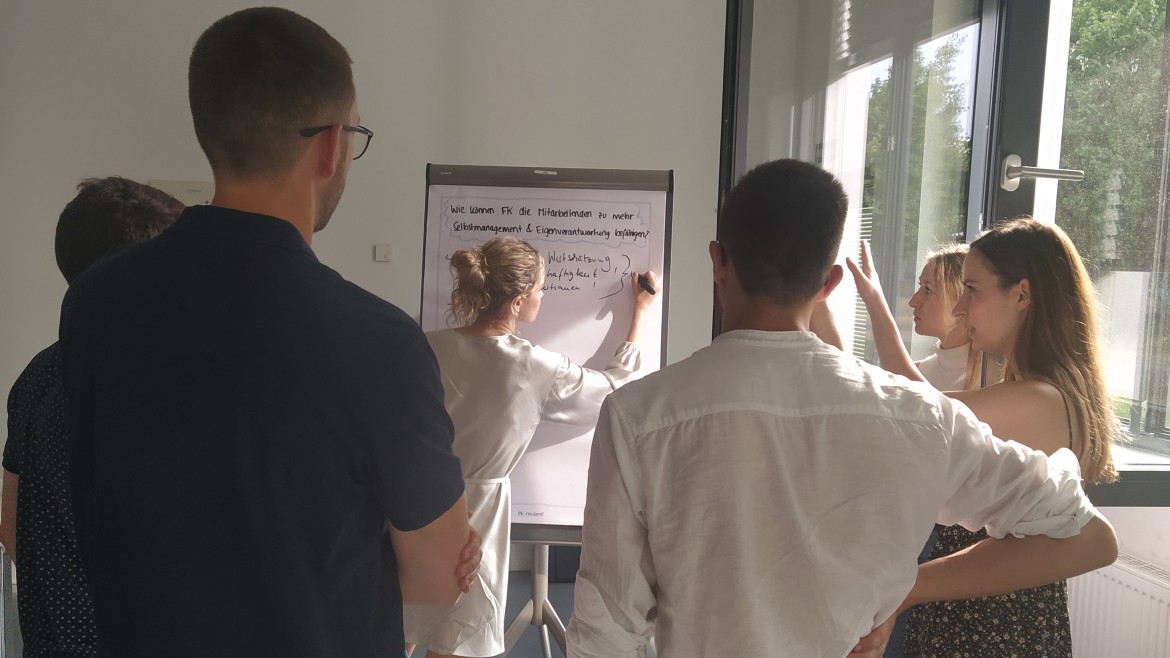 Eine Gruppe Studierender erarbeitet an einem Flipchart Antworten.