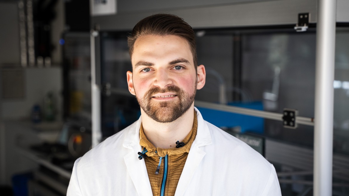 Wissenschaftlicher Mitarbeitr Patrik Hanisch lächelt in seinem Labor in die Kamera