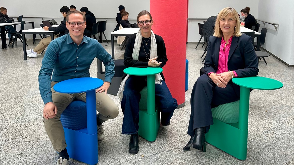HM-Kanzler Jörg Finger, Prof. Dr. Ruth Maria Otto und HM-Präsidentin Prof. Dr. Sonja Munz sitzen bei der Eröffnung des renovierten Lernzentrums auf neuen, bunten Drehstühlen mit integrierten Tischen.