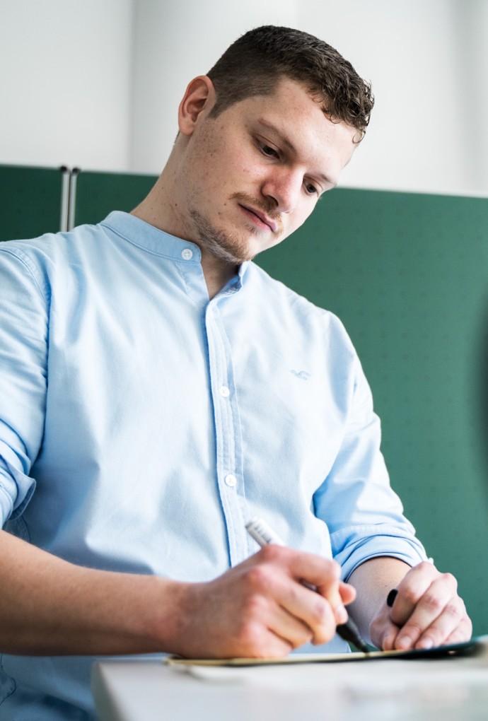 HM Mitarbeitender schreibt mit einem Stift auf ein Blatt Papier.