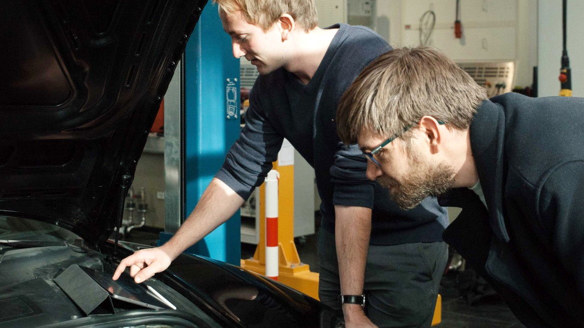 Zwei Ingenieure beugen sich über die geöffnete Motorhaube eines Fahrzeugs.