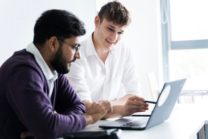 Zwei junge Männer sitzen gemeinsam vor einem Laptop und diskutieren.