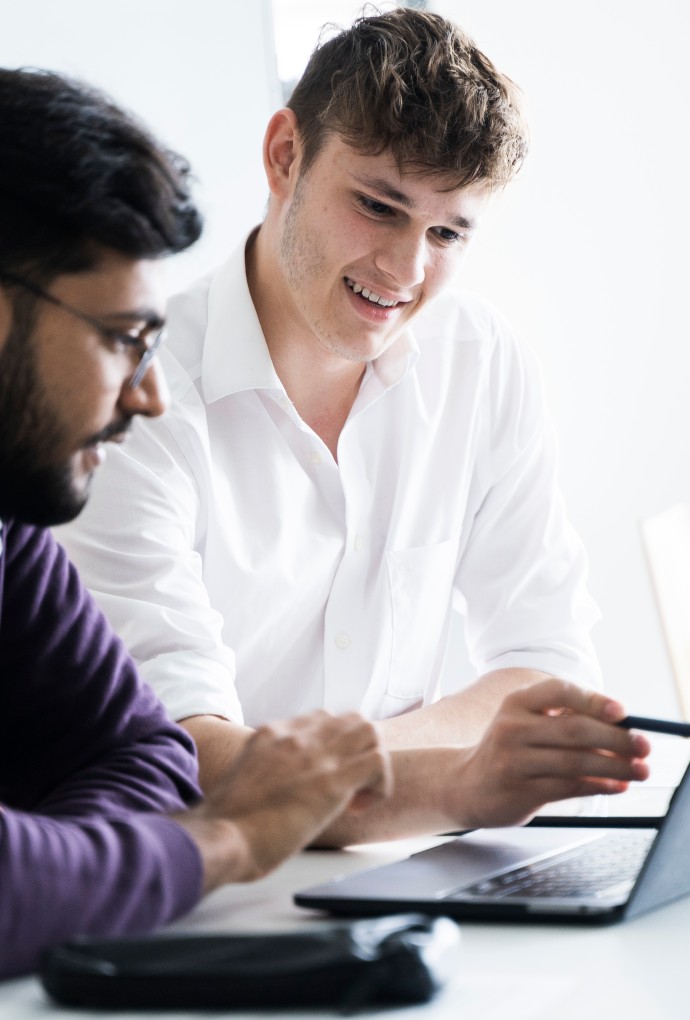 Zwei junge Männer sitzen gemeinsam vor einem Laptop und diskutieren.