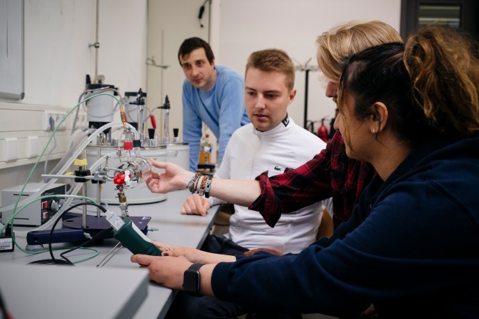 Wissenschaftliches Arbeiten (Foto: Ulrike Myrzik / Hochschule München) Promovierende betrachten einen Versuch.