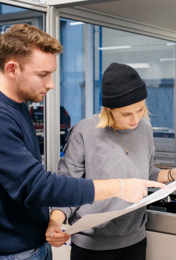 Gute Wissenschaftliche Praxis (© Hochschule München / Ulrike Myrzik ) Zwei Promovierende stehen vor einer technischen Anlage und betrachten einen Plan.