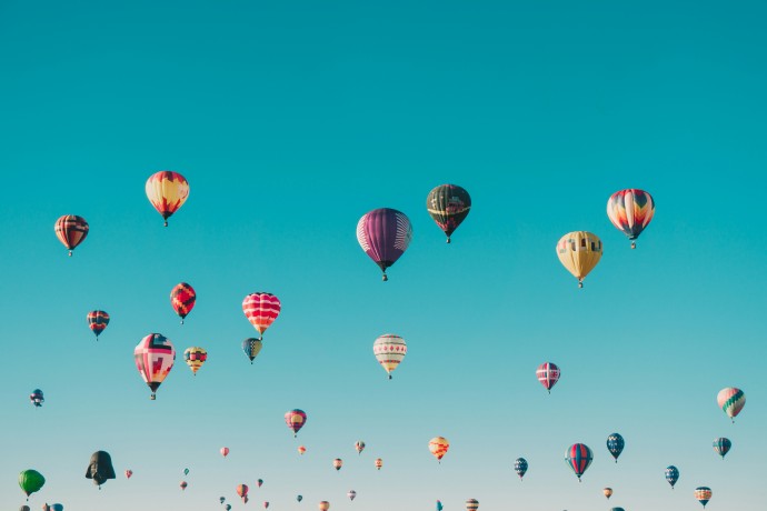 Vielle bunte Heißluftballone fliegen am blauen Himmel