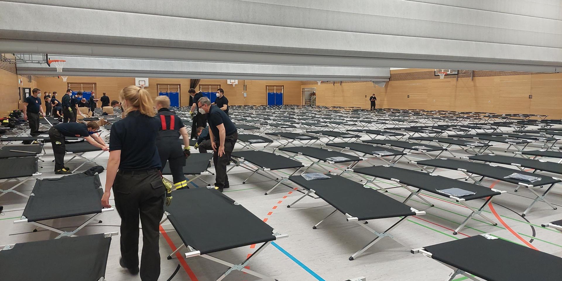 Foto Turnhalle mit aufgestellten Betten und Helferinnen und Helfern