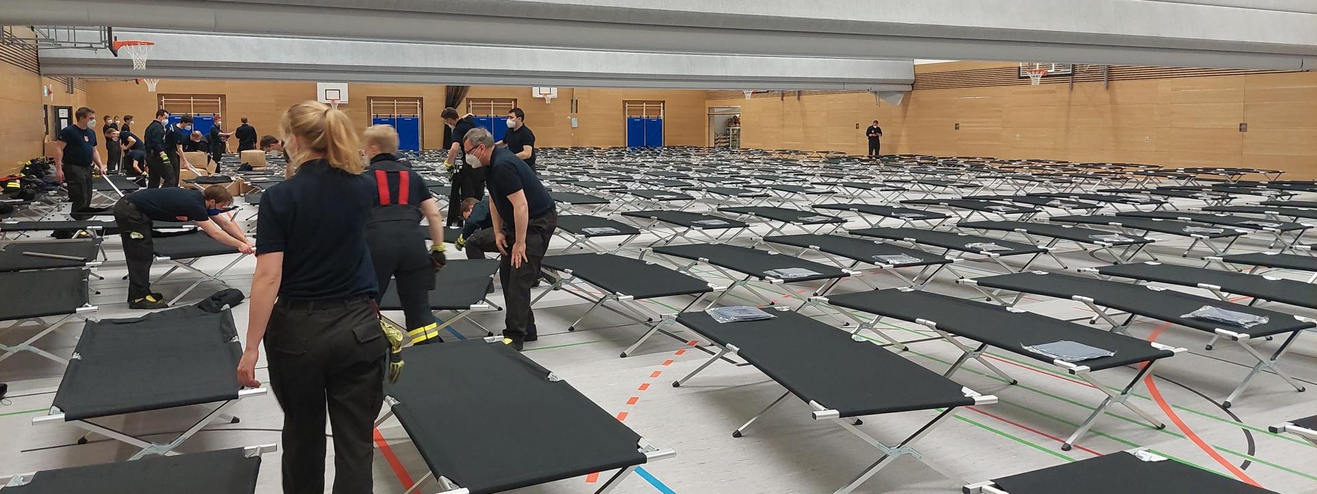 Foto Turnhalle mit aufgestellten Betten und Helferinnen und Helfern