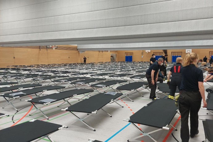 Foto Turnhalle mit aufgestellten Betten und Helferinnen und Helfern