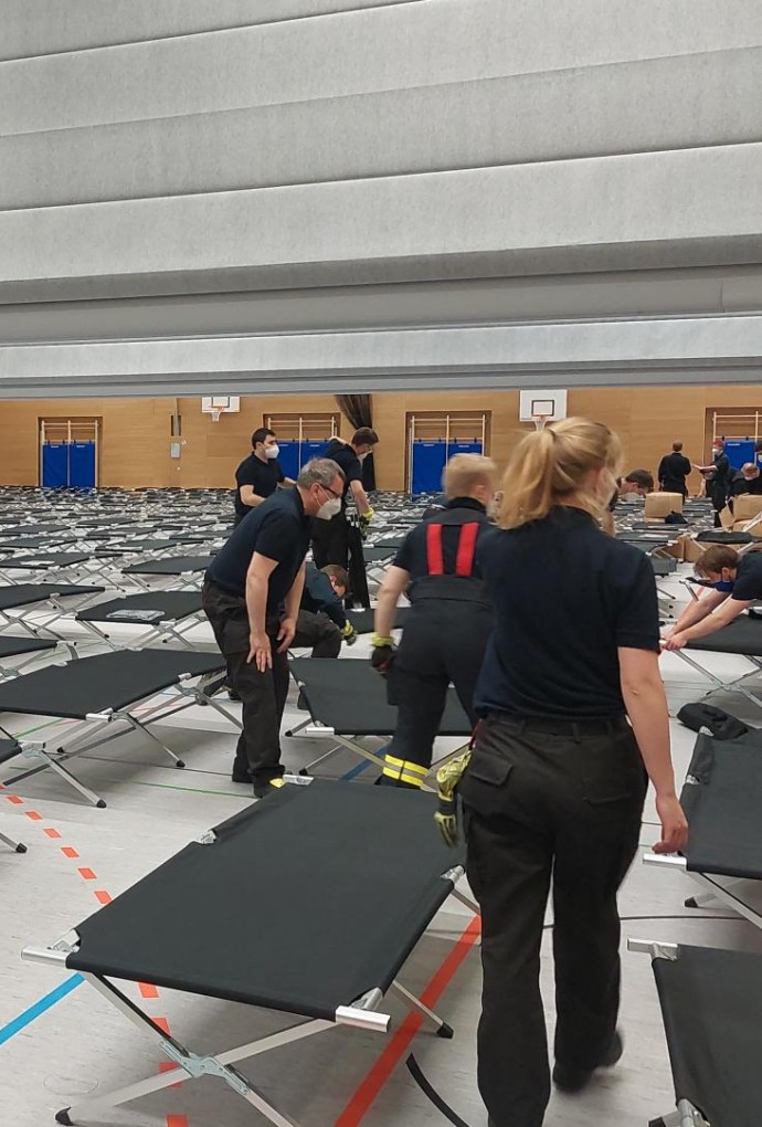 Foto Turnhalle mit aufgestellten Betten und Helferinnen und Helfern