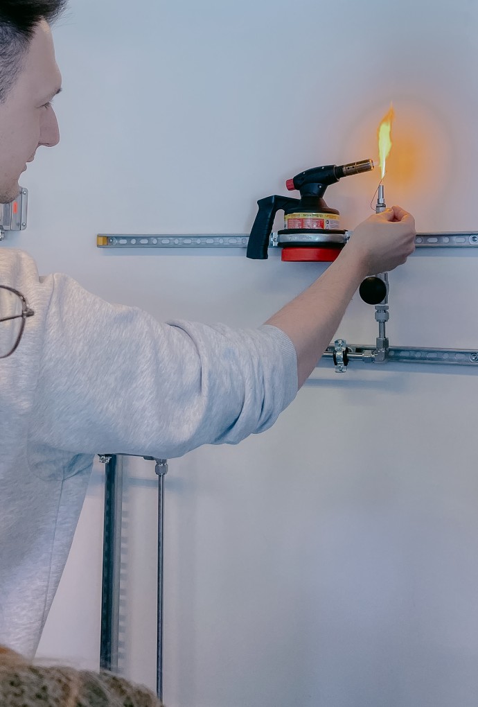 Studierender des FIT-Masters hält ein Feuerzeug an einen Gasbrenner, um das Gas sichtbarer zu machen