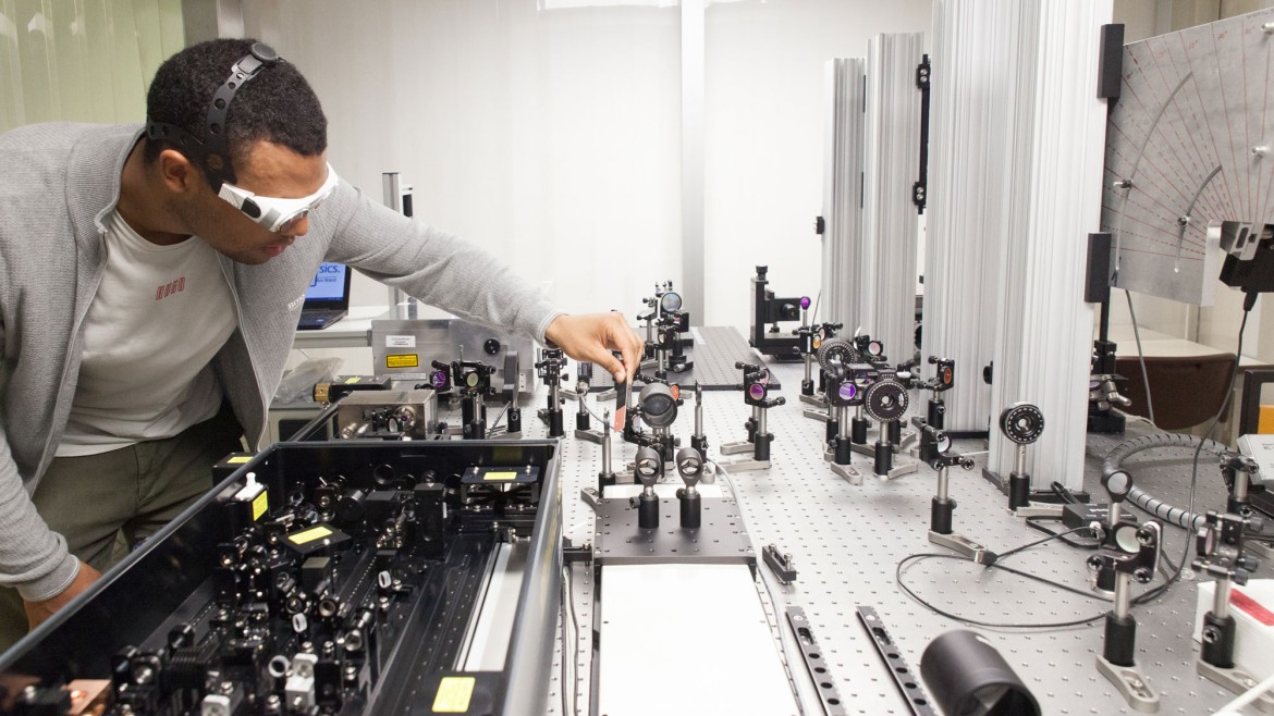 Student an einem optischen Tisch vor einem Praktikumsaufbau im Laserzentrum, Hochschule München
