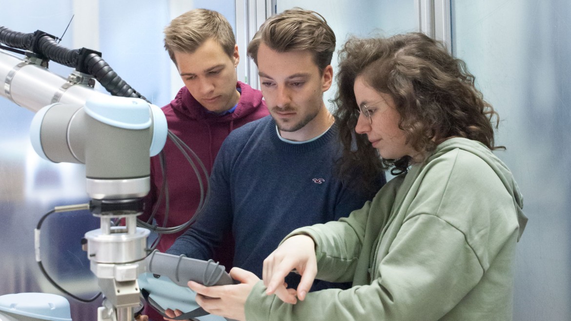 Drei Studierende mit einem Steuerelement für Roboter im Labor für Automatisierung und Robotik