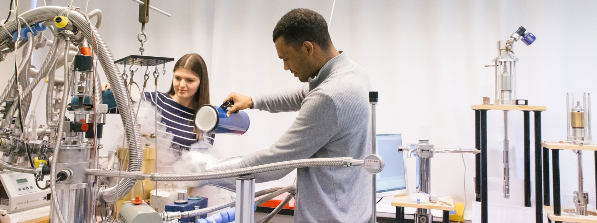 Zwei Studierende füllen Flüssigstickstoff in Behälter am Versuchsaufbau im Labor für Festkörperphysik