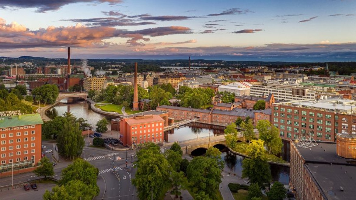 Das Bild zeigt die Innenstadt von Tampere in Finland mit verschiedenen Backsteinhäusern, Schornsteinen und dem Fluss Tammerkoski.