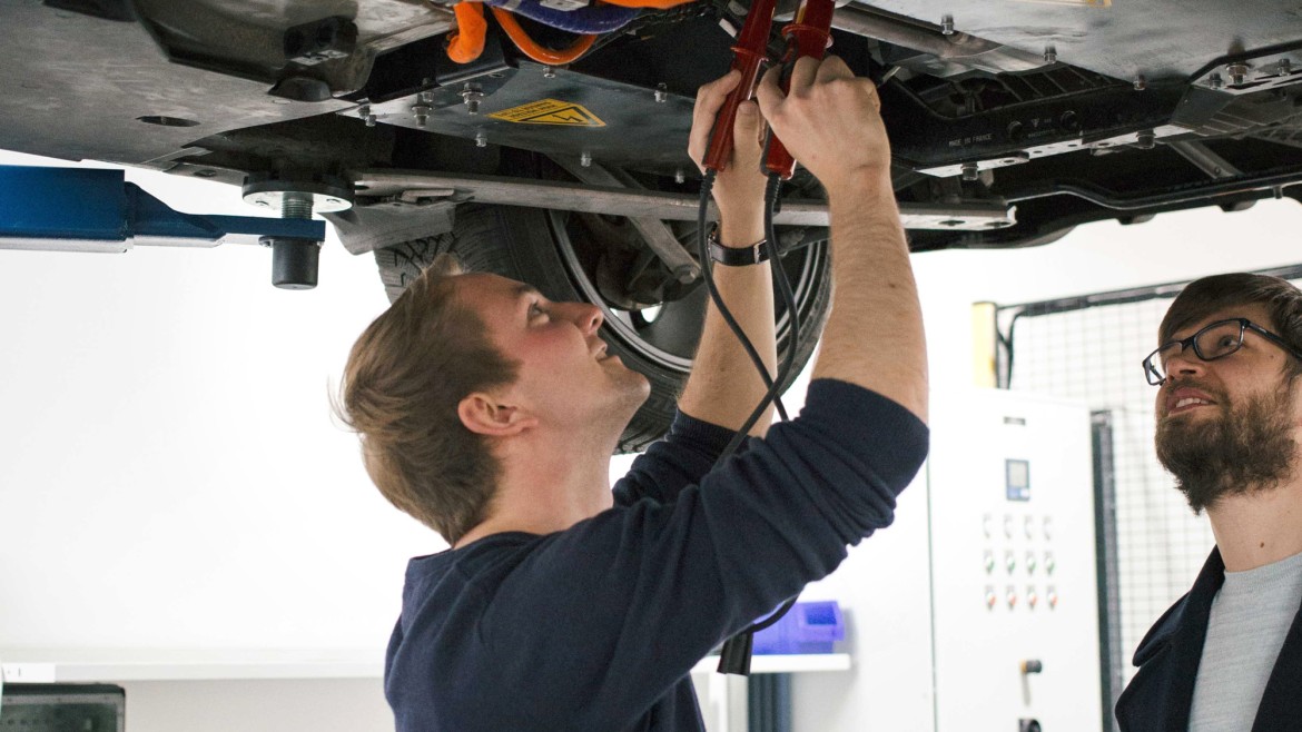 2 Personen arbeiten an einem aufgebockten Auto